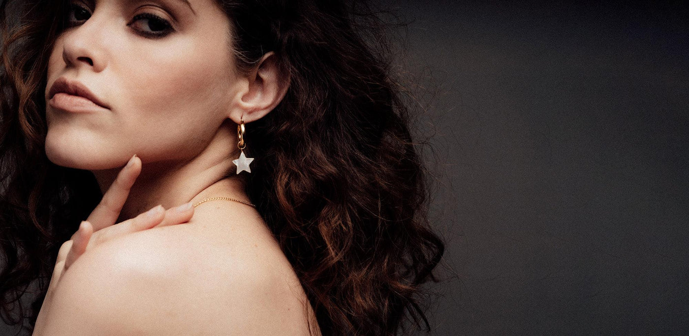 A woman on a black background wearing Freya Rose Star earrings from the Star and Moon Jewellery collection